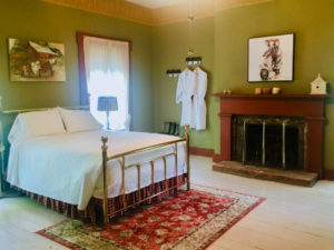 The Columbus Room, with a sage-green color scheme and brass bed, is pictured.